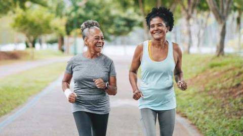 Two women of color walk side by side on a paved trail.